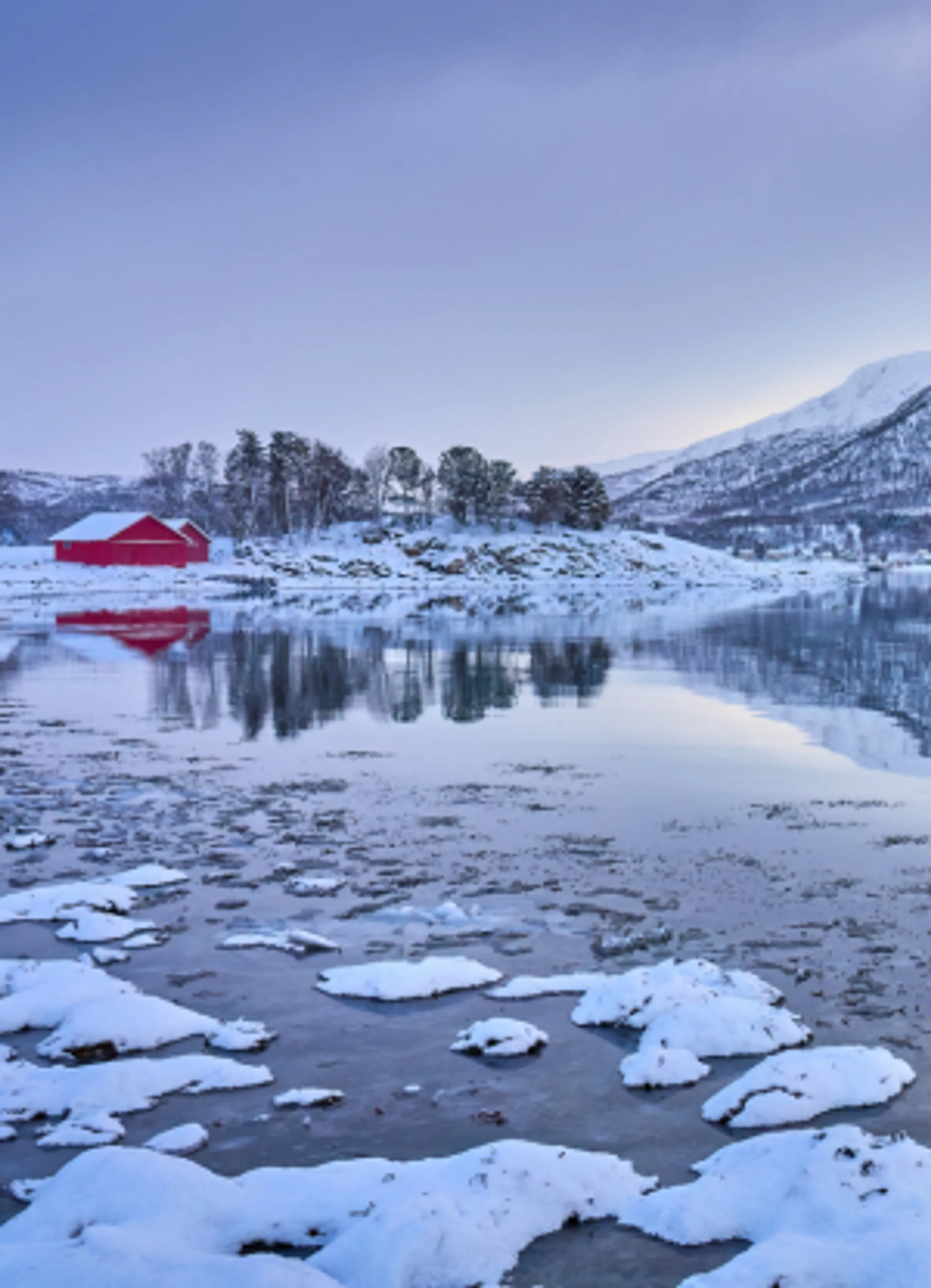 Fjord mit rotem Haus im Sonnenlicht im Winter in Nordnorwegen